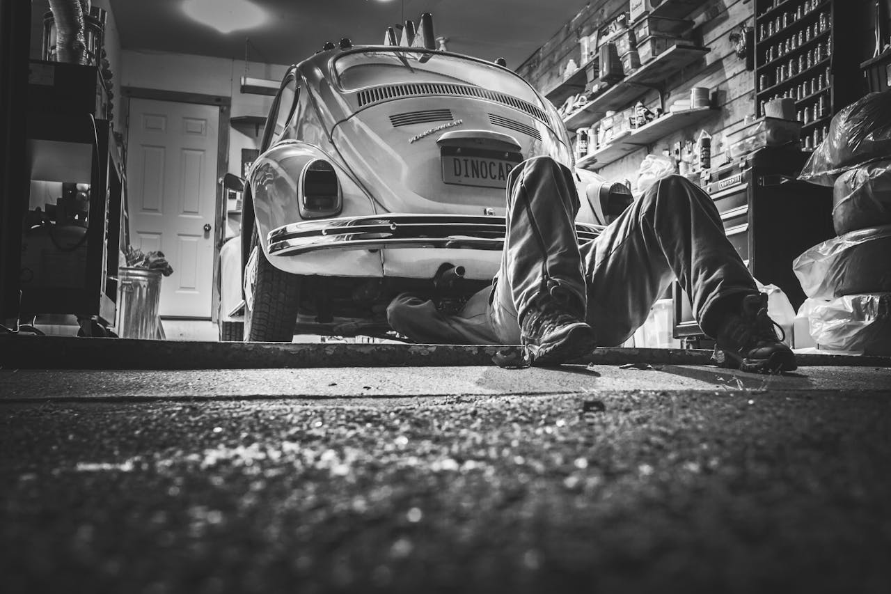 Mechanic working beneath a classic Volkswagen Beetle in a vintage garage setting.